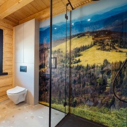 Jakub Matuszny jamafoto.pl - Nowoczesna łazienka z kabiną prysznicową z czarnymi ramami i fototapetą górskiego krajobrazu, drewniane ściany w stylu góralskim, wisząca toaleta i jasna podłoga z lastryko.