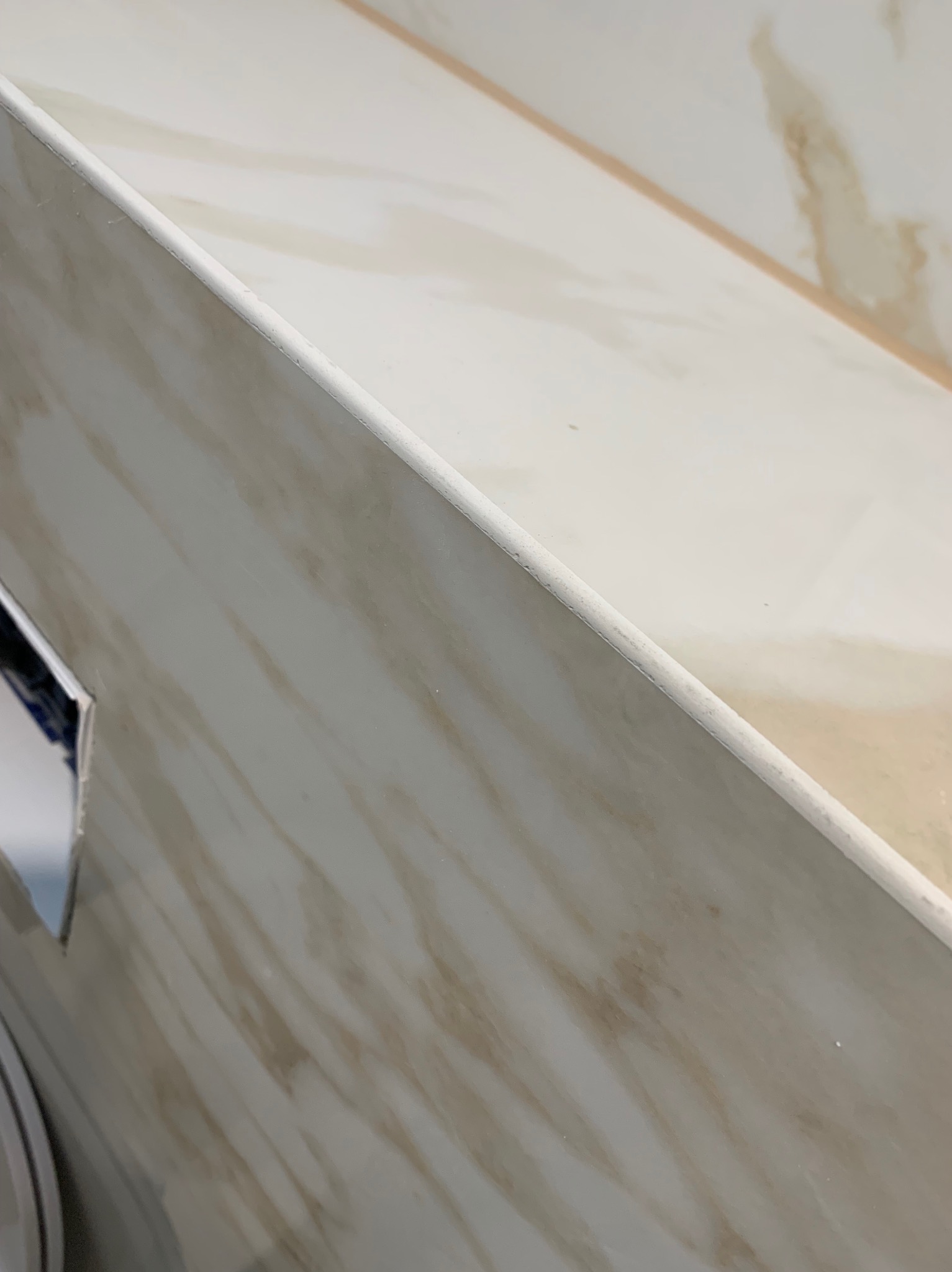 Fragment wykończonej ściany i blatu z płyty imitującej marmur w odcieniach beżu i bieli, widoczne delikatne żyłki i gładka powierzchnia.