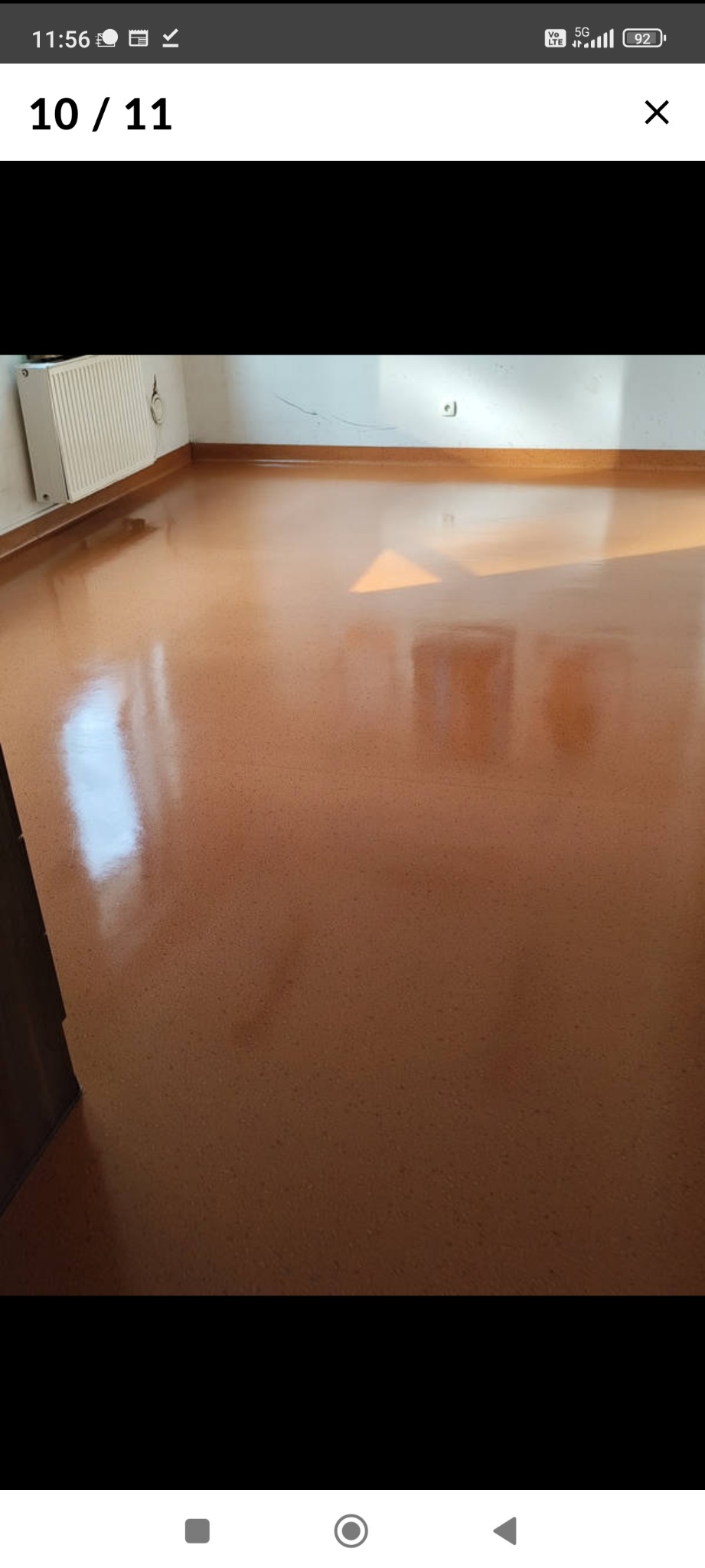 Błyszcząca, brązowa podłoga w pustym pokoju z grzejnikiem i listwami przypodłogowymi, odbijająca światło słoneczne.