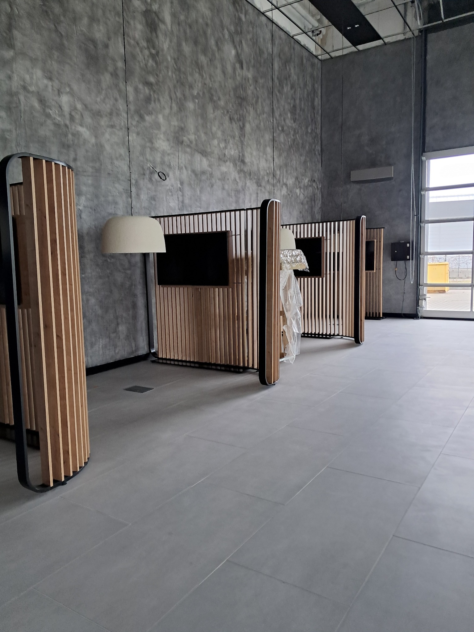 Nowoczesne, minimalistyczne biuro w Bydgoszczy z drewnianymi panelami działowymi i szarą betonową ścianą, w trakcie sprzątania lub przygotowania do użytku.