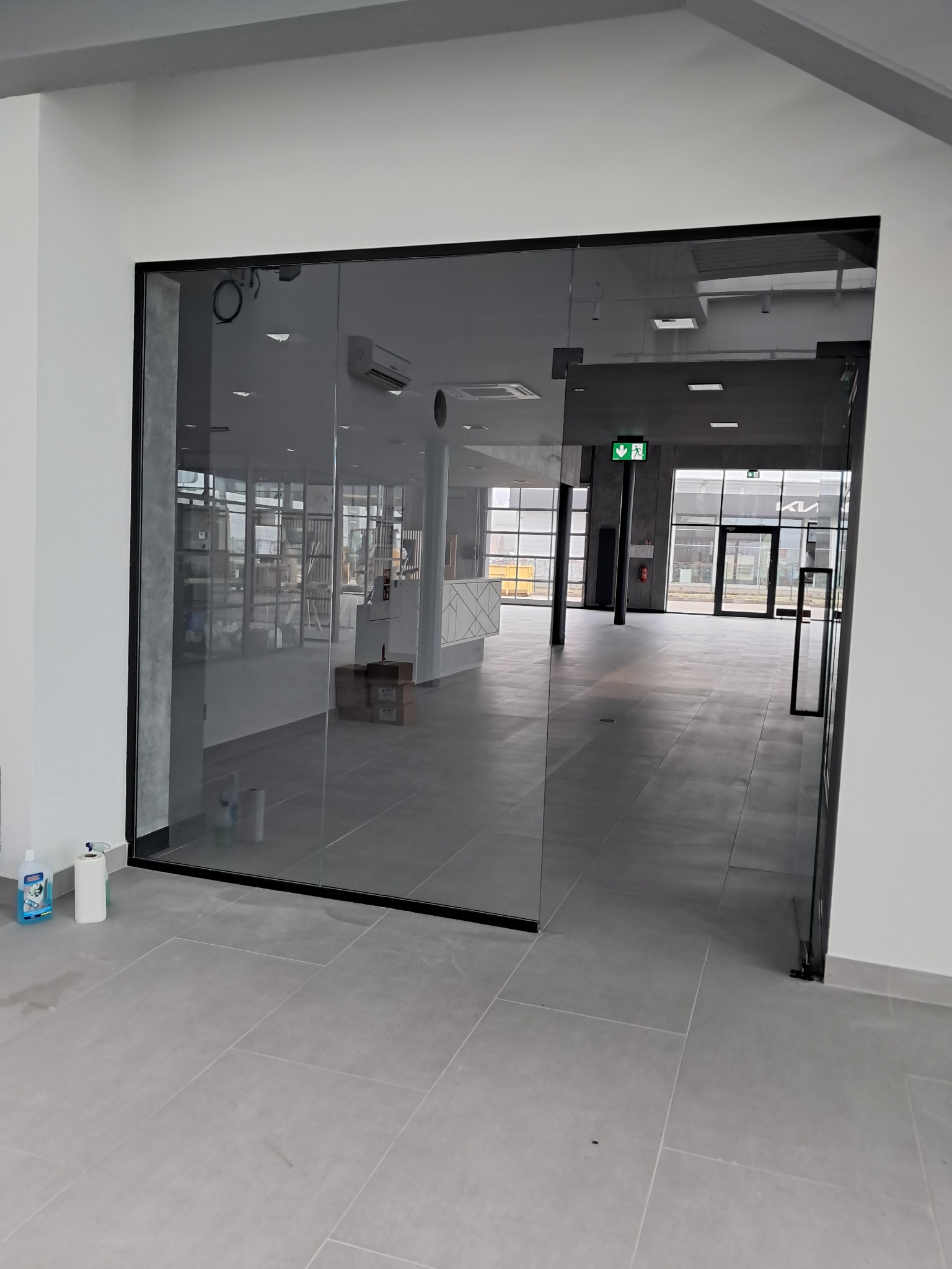 Wnętrze biura z przeszkloną ścianą, na podłodze widoczne ślady po czyszczeniu, obok ściany stoją środki czystości.