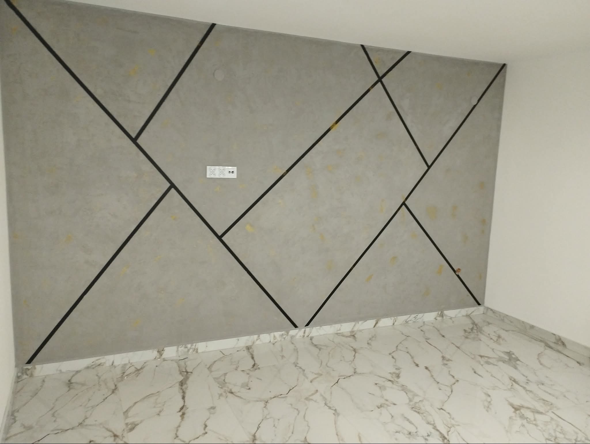 Ściana z dekoracyjną szarą fakturą i czarnymi liniami tworzącymi geometryczny wzór, gniazdko elektryczne, marmurowe płytki podłogowe. Wykończenie wnętrza.