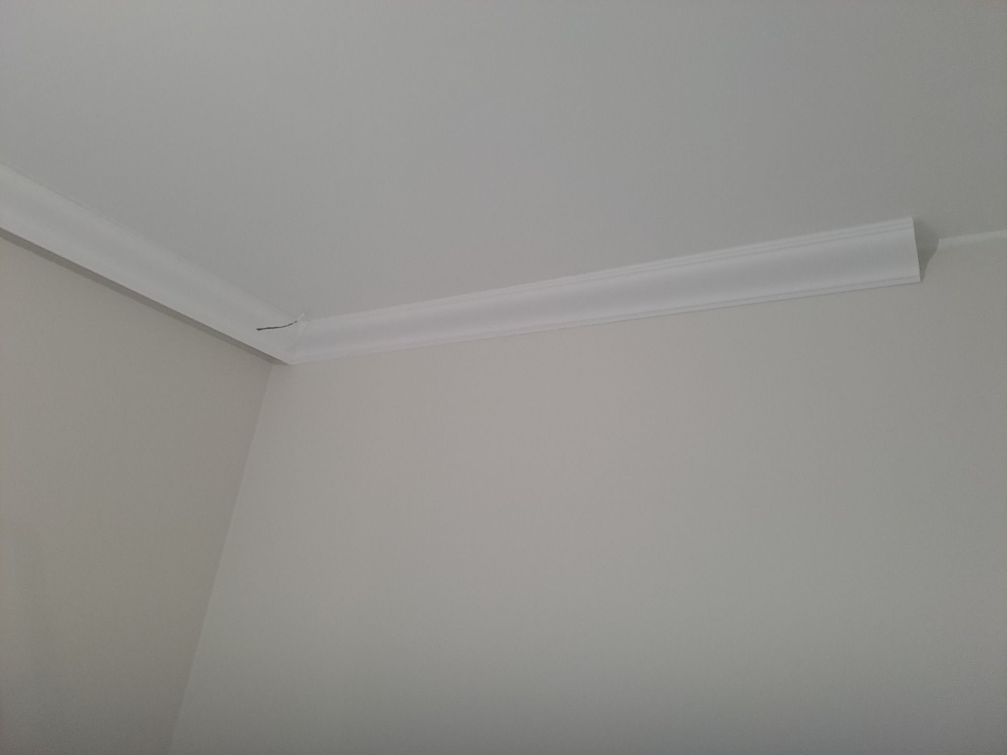 Fragment narożnika pokoju z zamontowaną białą listwą dekoracyjną przy suficie, widoczny minimalny ubytek w narożniku listwy.