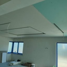BUDMASTER Ivan Guivan - Montaż sufitu podwieszanego z płyty karton gips w pomieszczeniu z oknem, widoczne profile i kable elektryczne.