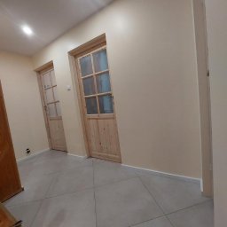 YEVHENII SEMENOV - Korytarz po odnowieniu z dwiema drewnianymi drzwiami z szybami, świeżo pomalowanymi ścianami w odcieniu beżu i nową, szarą podłogą z płytek.