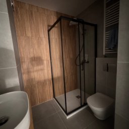 YEVHENII SEMENOV - Nowoczesna łazienka z kabiną prysznicową w czarnej ramie, umywalką nablatową i drewnopodobną okładziną ściany. Minimalistyczny design, szare płytki podłogowe.