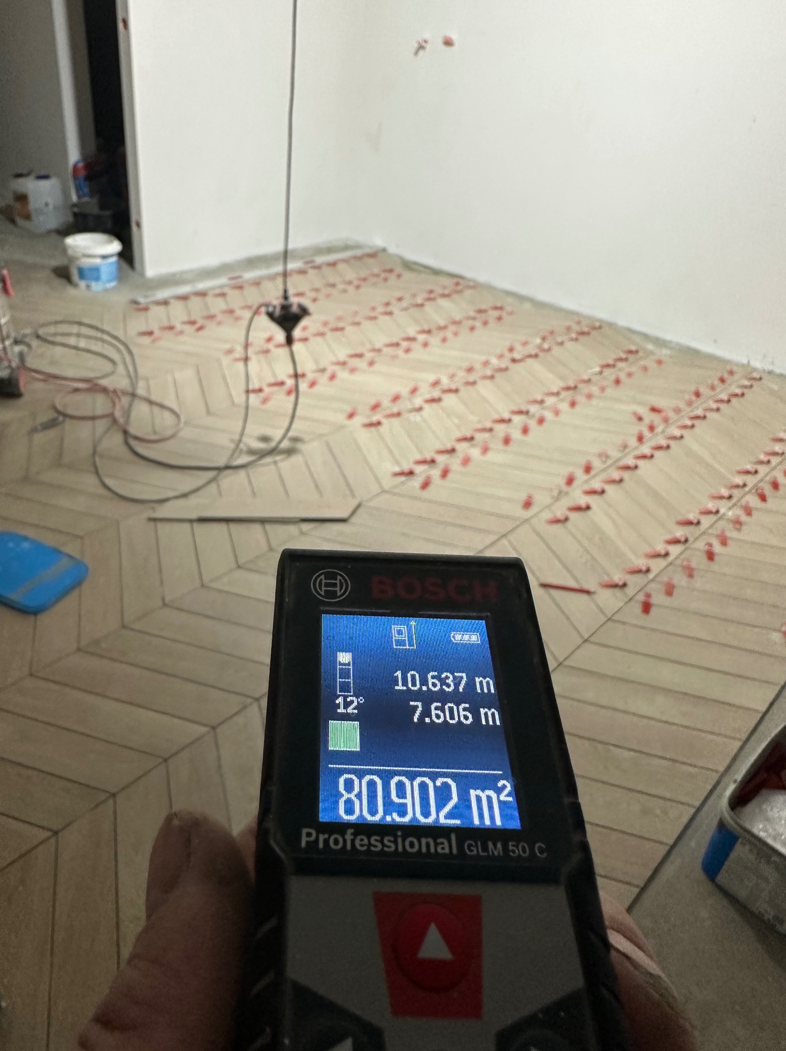 Pomiar powierzchni parkietu ułożonego w jodełkę, wykonany laserowym miernikiem odległości Bosch GLM 50 C, z widocznymi krzyżykami dystansowymi.