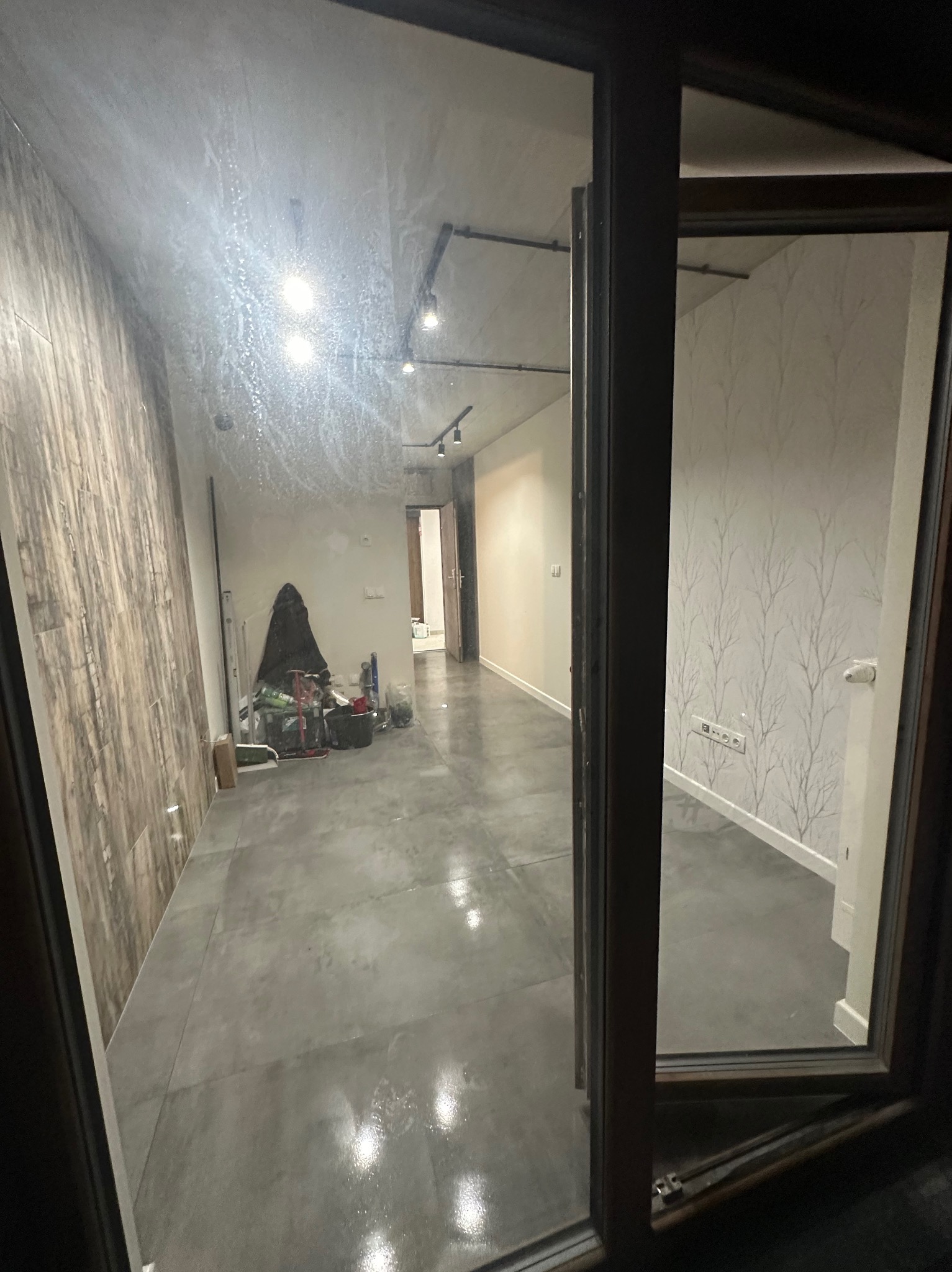 Wnętrze mieszkania w Szczecinie w trakcie prac wykończeniowych, widok przez okno z widocznymi narzędziami i materiałami budowlanymi w tle.