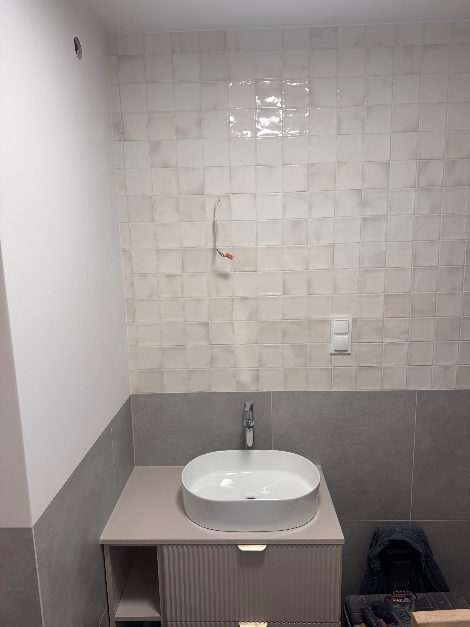 Jasna łazienka po remoncie: białe, kwadratowe płytki na ścianie, umywalka nablatowa na szafce z frezowanymi frontami. Widoczne narzędzia.