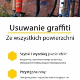 Pracownik w pomarańczowym kombinezonie usuwa graffiti z ceglanej ściany za pomocą specjalistycznego sprzętu podłączonego do przemysłowego odkurzacza.