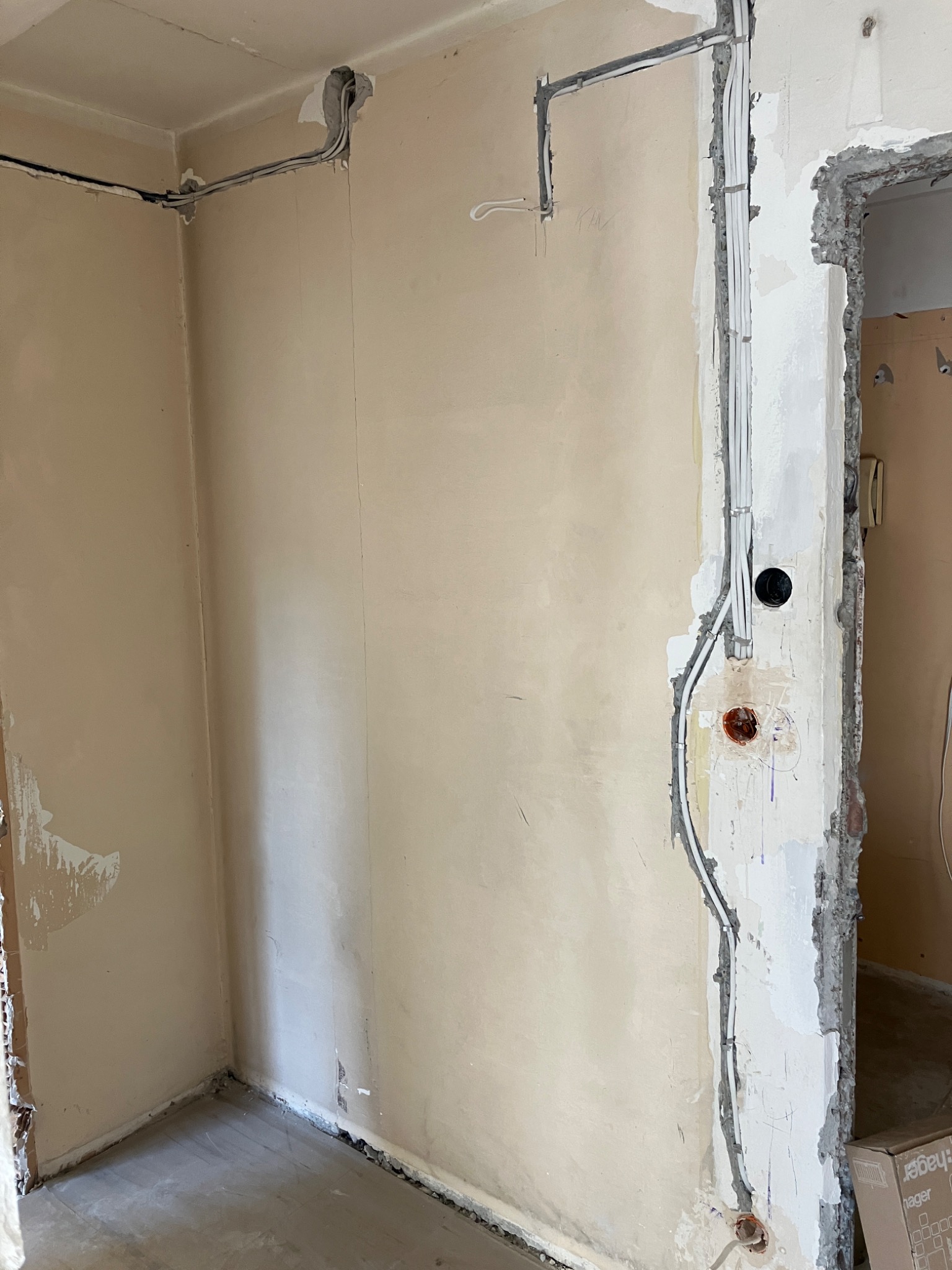 Wnętrze w trakcie remontu, widoczne kable elektryczne prowadzone po ścianach, częściowo w korytach, z przygotowanymi otworami pod gniazdka i włączniki, ściany w stanie surowym.