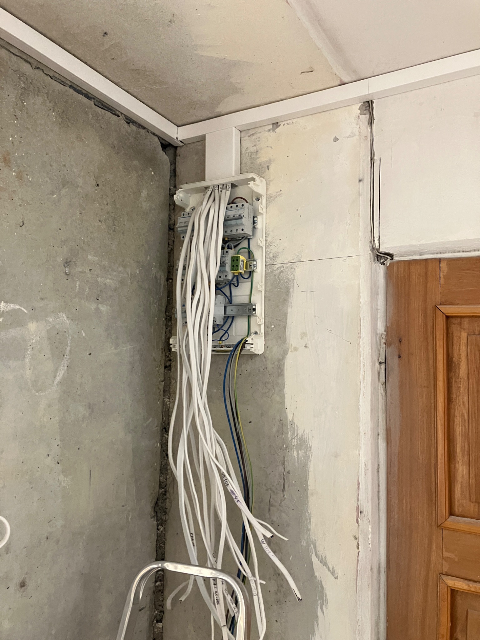 Rozdzielnica elektryczna z podłączonymi przewodami w surowym wnętrzu, widoczne przewody opisane markerem, ściany w stanie deweloperskim.