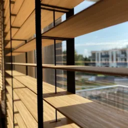 Drewniane żaluzje poziome z czarnymi elementami mocującymi, widok z bliska na tle budynku i błękitnego nieba.