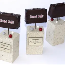 Trzy statuetki z motywem walizki, każda na kamiennej podstawie z grawerowaną tabliczką z podziękowaniami na rok 2025, z akcentami w postaci kulek.