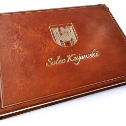 KSIĘGA PAMIĄTKOWA SKÓRZANA Z HERBEM MIASTA SOLEC KUJAWSKI. Księga ręcznie uszyta z 150 kart o gramaturze 170, oprawiona w skórę naturalną, proste linie złote i ślepe, tłoczenie złotem herbu miasta, narożniki mosiężne. Prostota i elegancja. KSIĘGI PIMAX