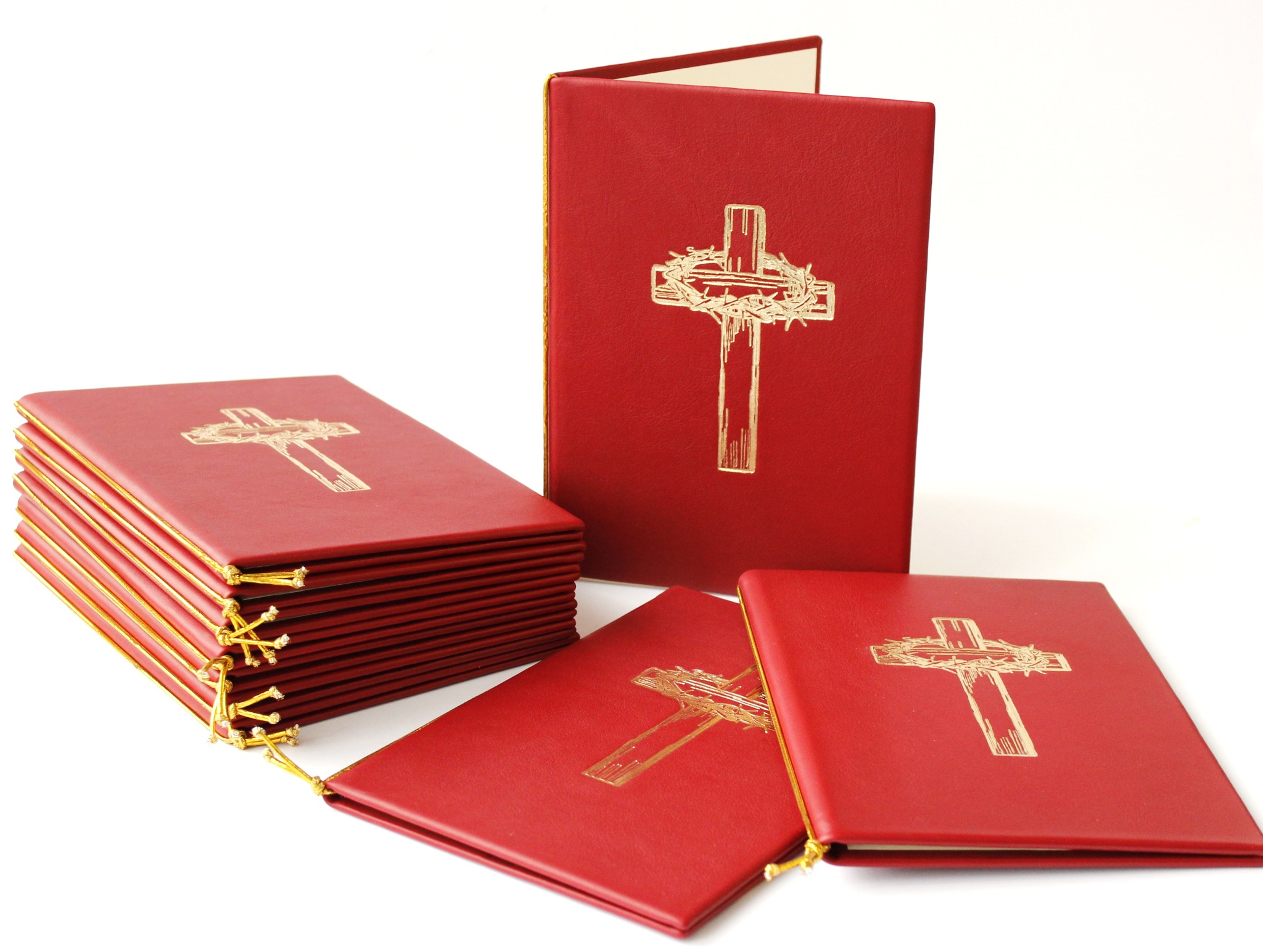 Czerwone, skórzane okładki na śpiewniki z tłoczonym złotym motywem krzyża z koroną cierniową. Widoczny stos okładek i pojedyncze egzemplarze na białym tle.