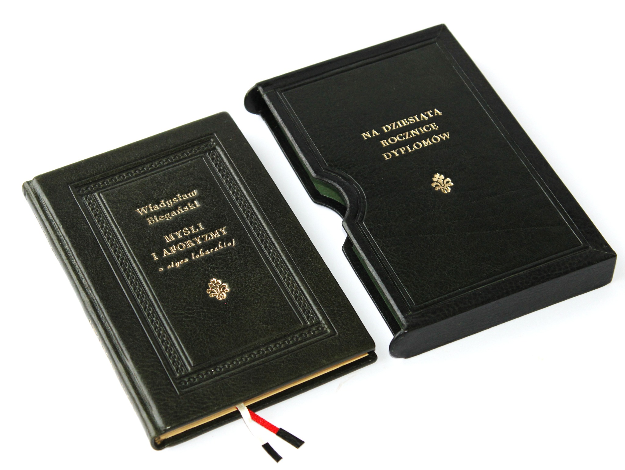 Książka w skórzanej, ciemnozielonej oprawie z tłoczeniami, leżąca obok dopasowanego etui. Widoczne złote napisy i zakładka z tasiemkami w kolorach flagi Polski.