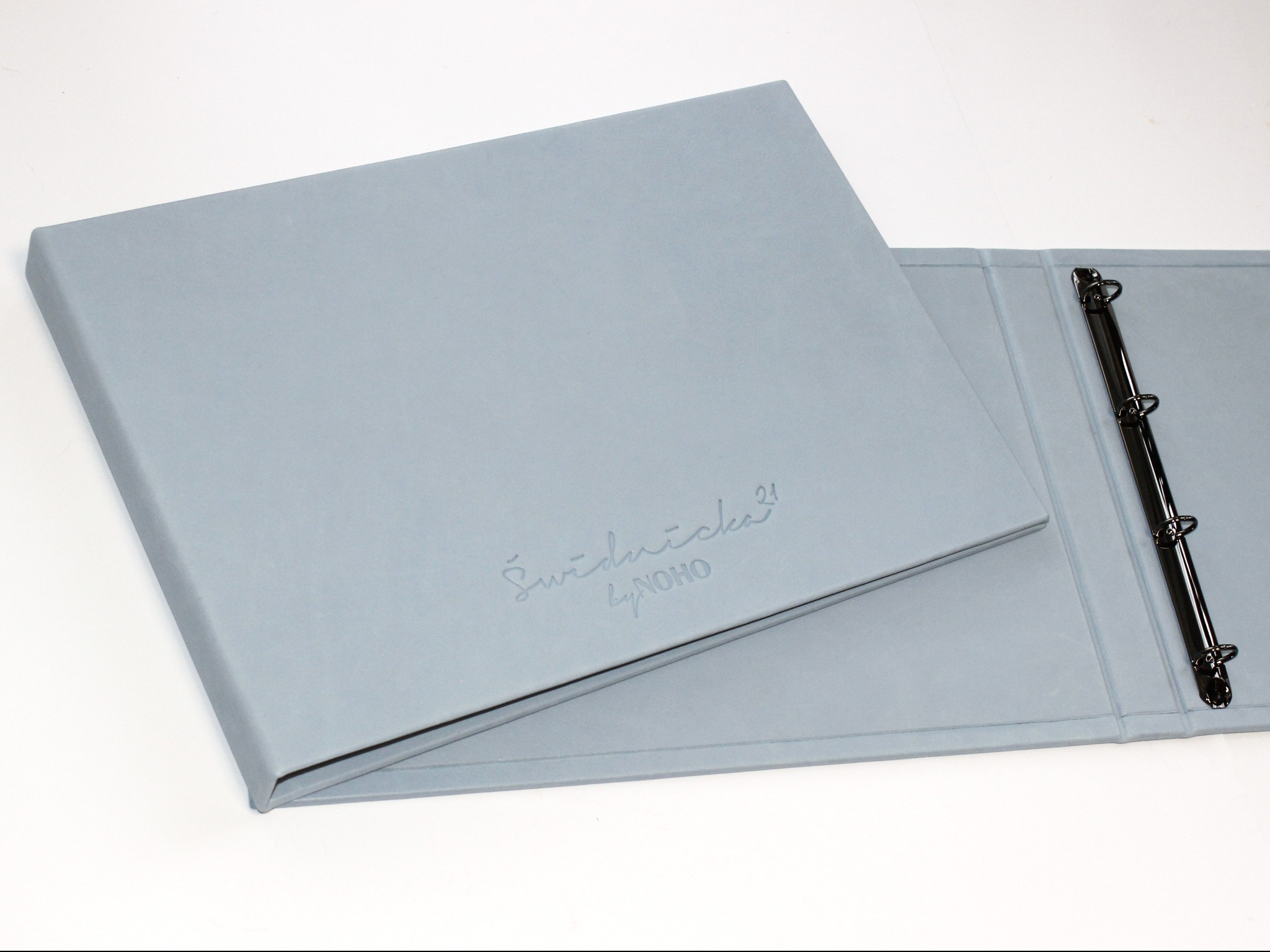 Otwarty, szary segregator ringowy z tłoczonym logo na okładce, leżący na białym tle. Widoczny mechanizm ringowy wewnątrz. Elegancki i minimalistyczny design.