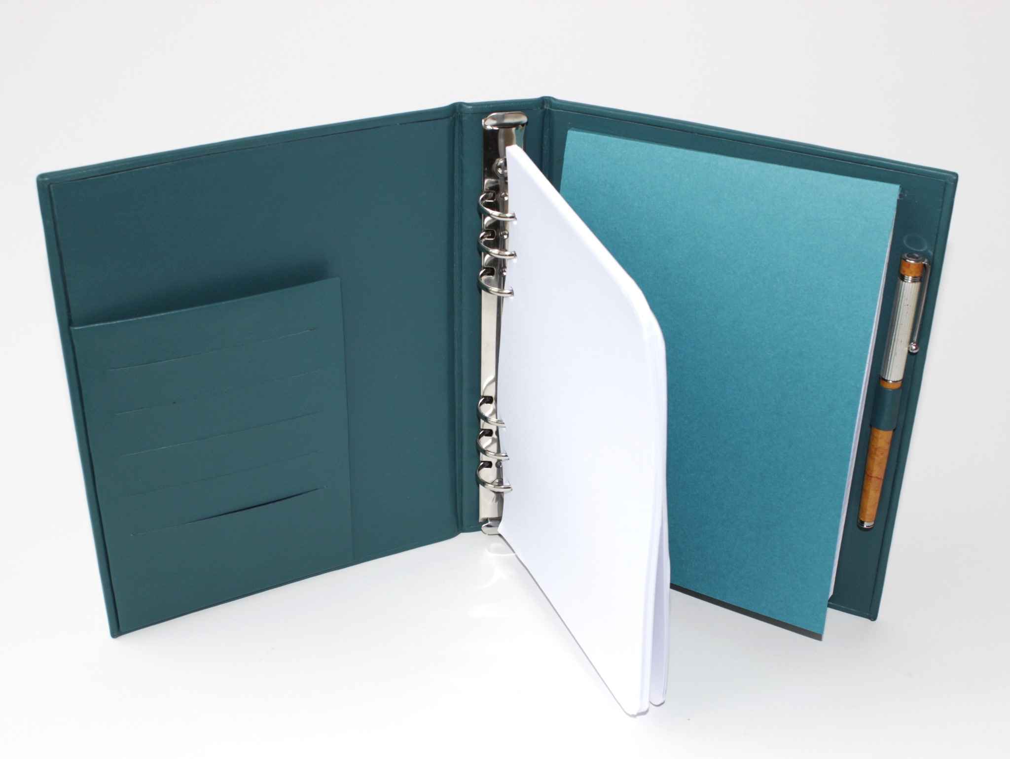 Otwarty, turkusowy organizer skórzany z metalowymi ringami, białymi kartkami i piórem. Wnętrze z kieszeniami na dokumenty. Ręcznie wykonany, elegancki design.