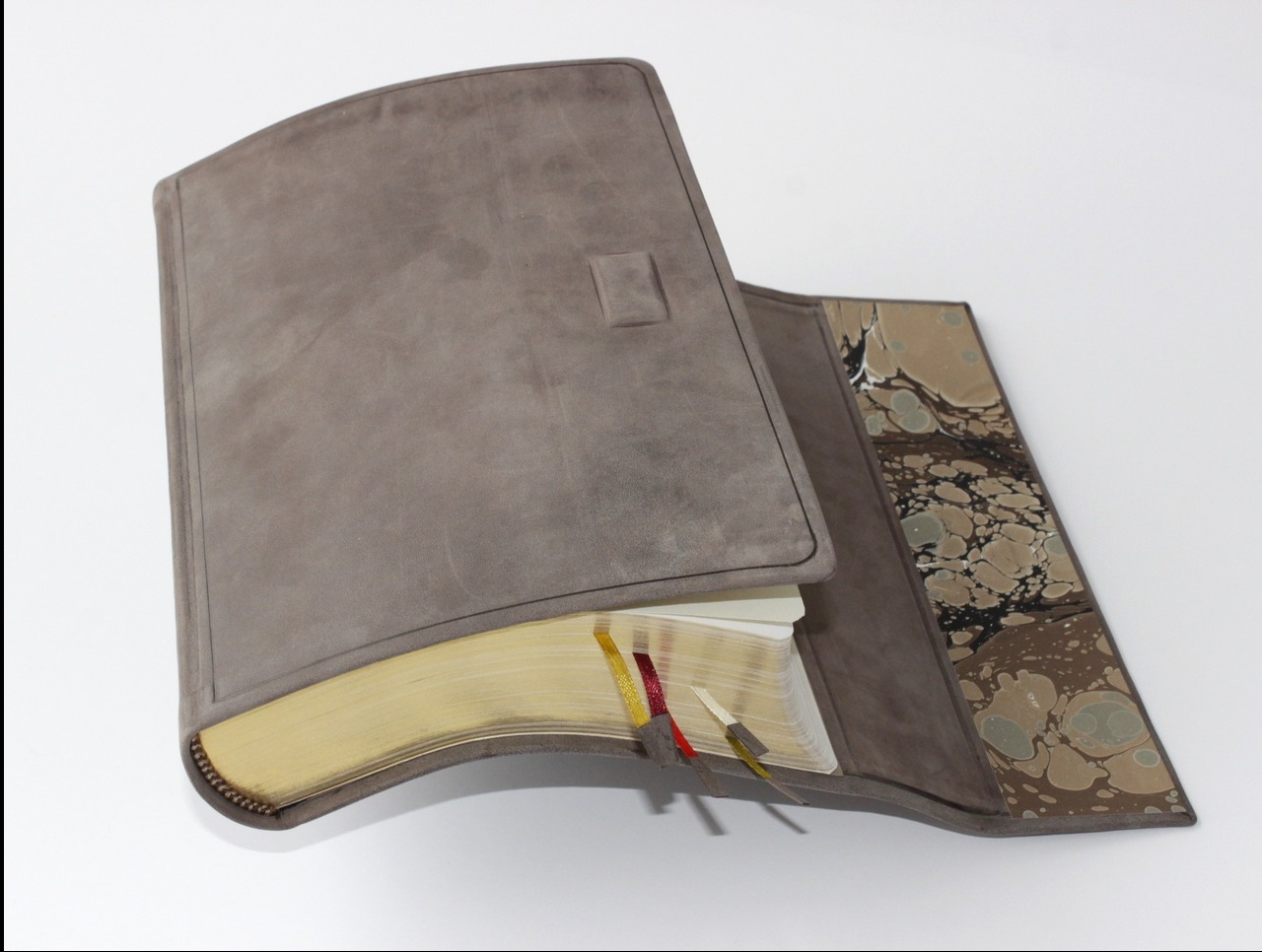 Ręcznie oprawiona Biblia w elastycznej, szarej skórze z marmoryzowanymi wyklejkami i złoconymi brzegami kartek. Widoczne tasiemki-zakładki i zapięcie na magnes.