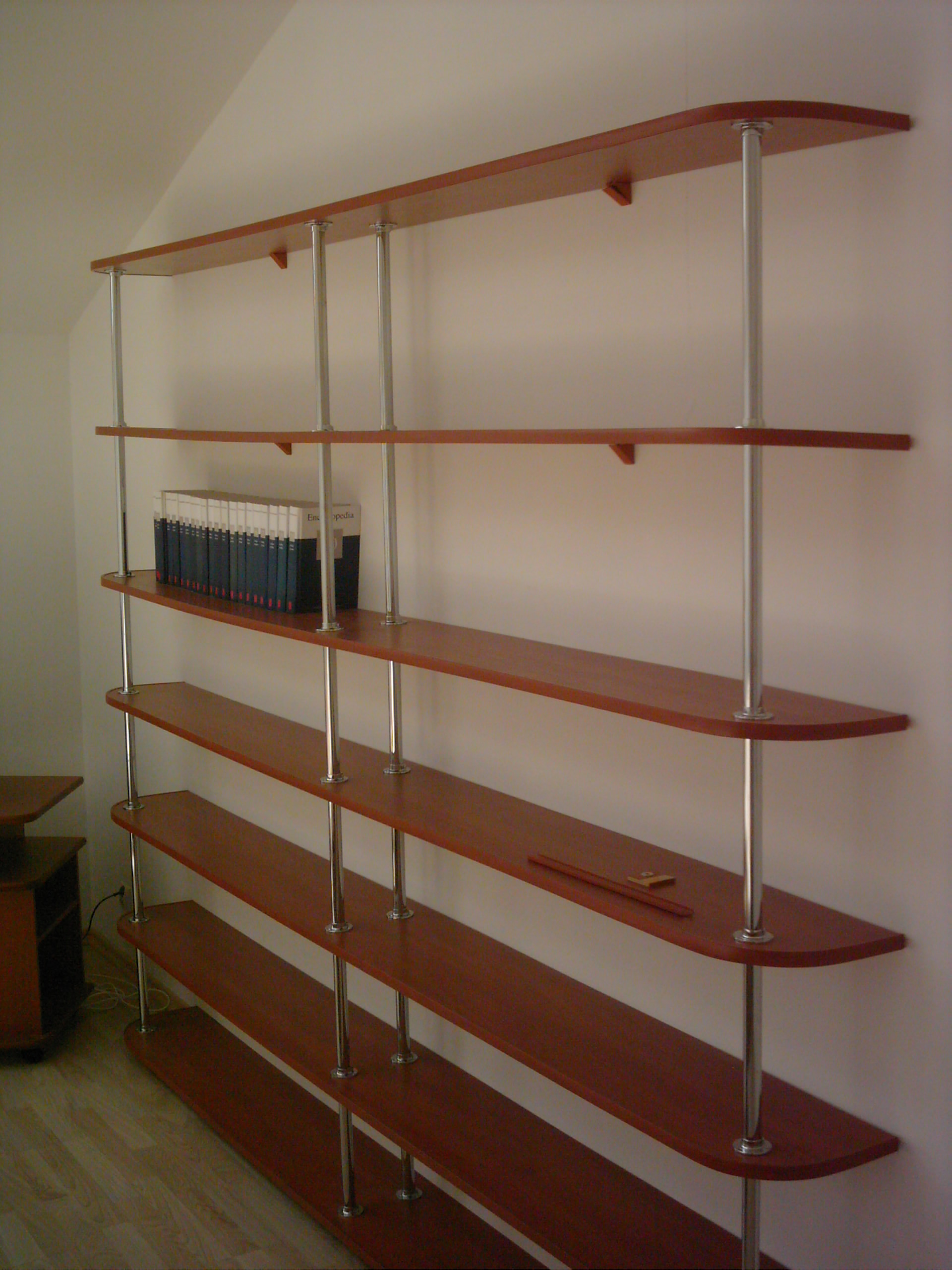 Regał na wymiar z półkami z drewna w kolorze wiśni, wsparty na metalowych, chromowanych rurach, z książkami na jednej z półek i ołówkiem na innej, ustawiony na tle białej ściany w pokoju na poddaszu.