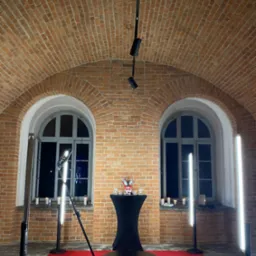 Okrągła platforma z czerwonym oświetleniem LED na czerwonym dywanie, otoczona lampami LED, ustawiona w ceglanym wnętrzu z łukowymi oknami i świecami.