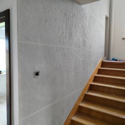 Usługi remontowo budowlane MAGBET - Ściana wykończona szarą gładzią dekoracyjną z widocznym gniazdkiem elektrycznym i fragmentem drewnianych schodów w trakcie remontu.