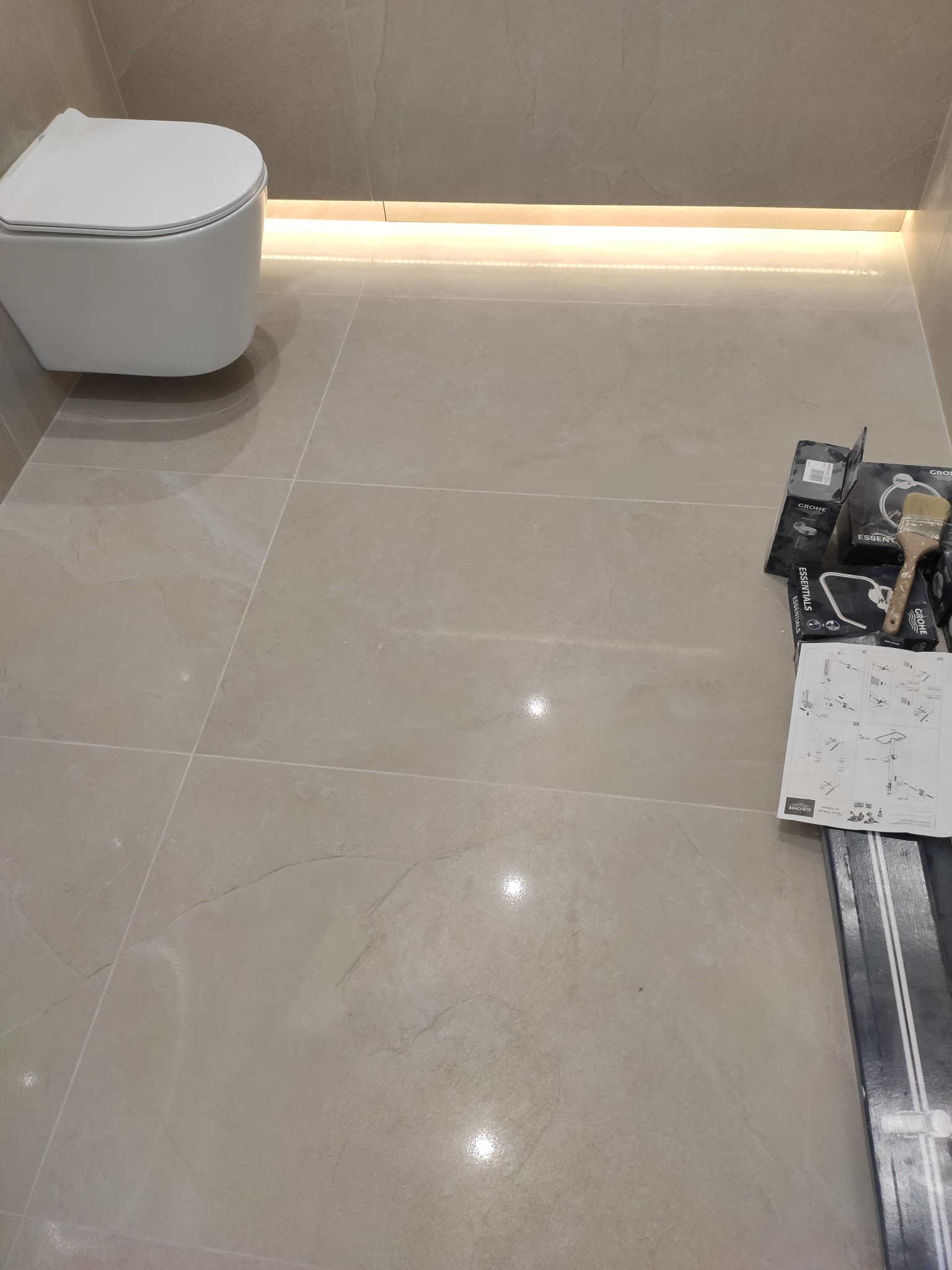 Podwieszana toaleta na szarej płytce z oświetleniem LED, obok akcesoria montażowe Grohe i instrukcja instalacji.
