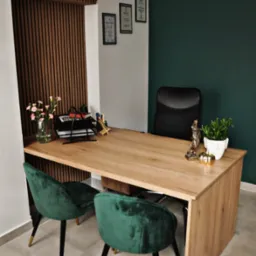 Nowoczesne biuro: drewniane biurko z zielonymi krzesłami, statuetka Temidy, kwiaty w wazonie, dyplomy na ścianie, zielona ściana w tle.