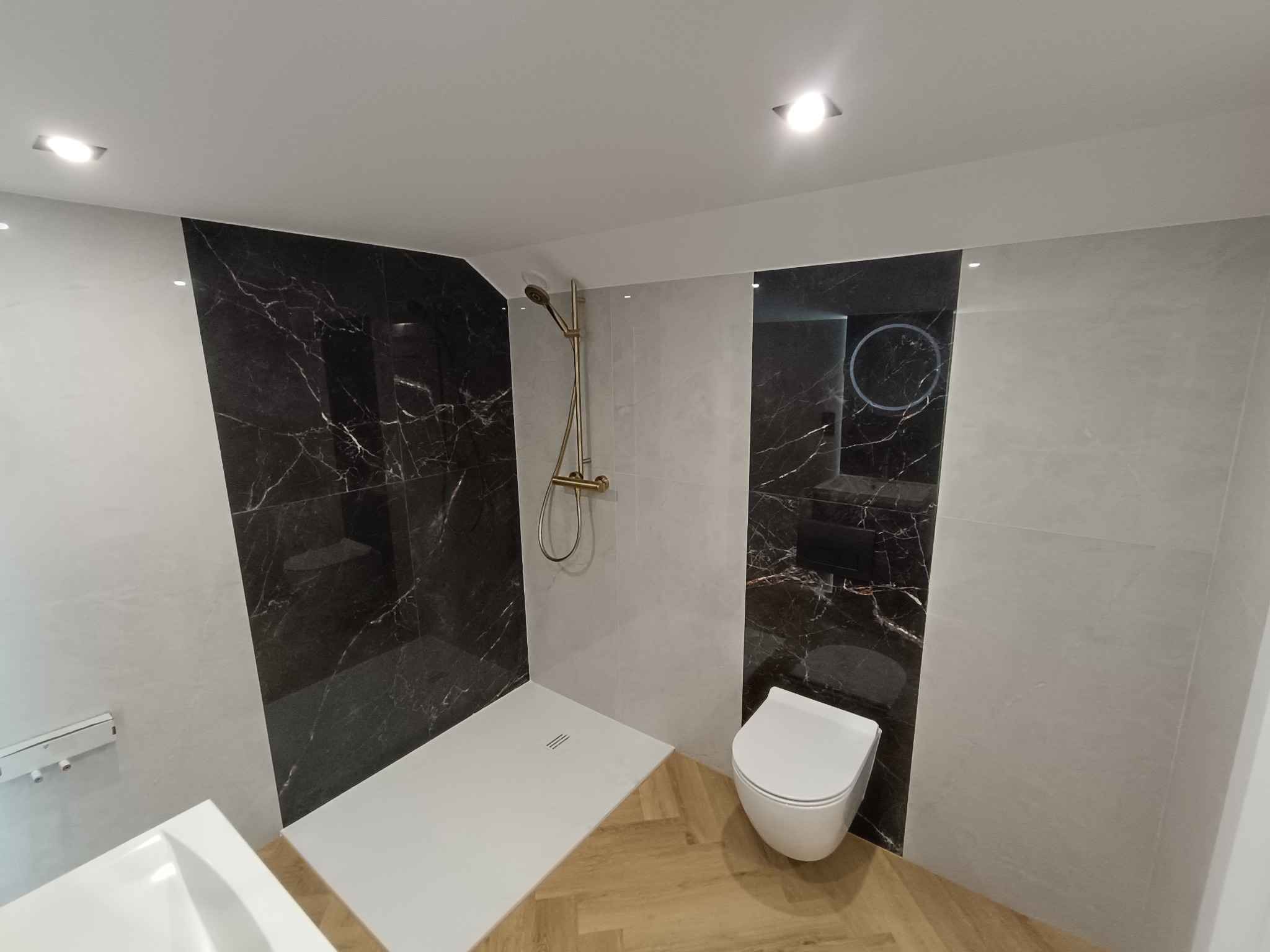 Nowoczesna łazienka z czarnymi płytkami imitującymi marmur, kabiną prysznicową typu walk-in i drewnopodobną podłogą ułożoną w jodełkę. Minimalistyczny design.