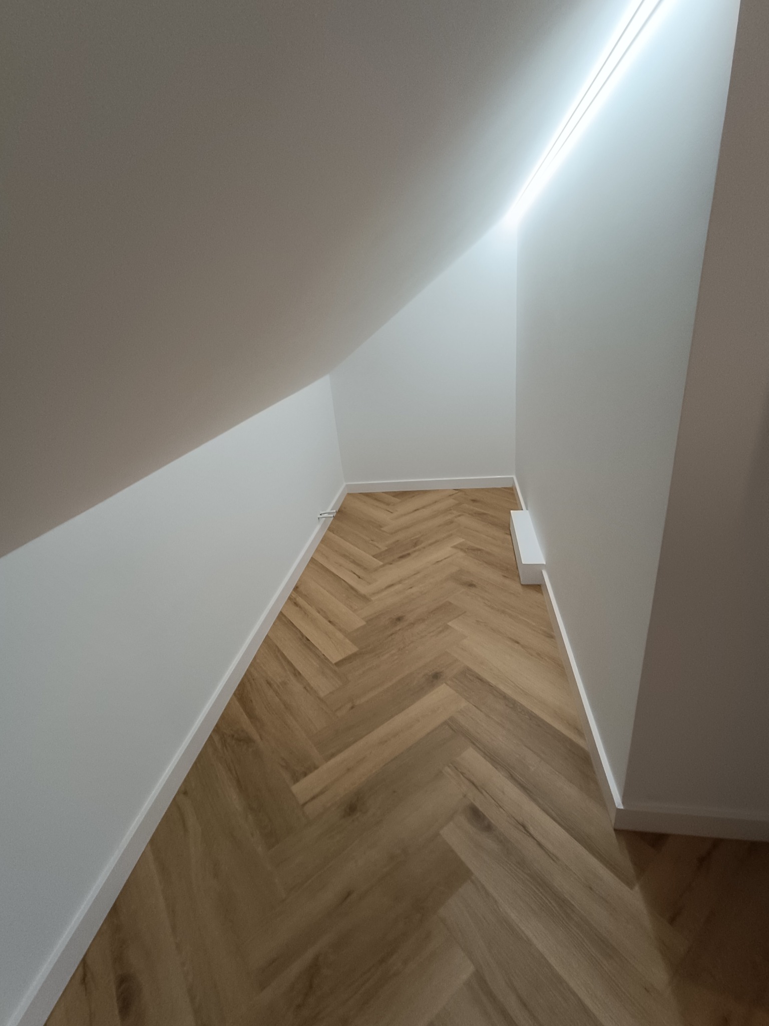 Wykończone poddasze ze skośnym sufitem, oświetleniem LED i parkietem ułożonym we wzór jodełki. Białe ściany i listwy przypodłogowe podkreślają nowoczesny charakter wnętrza.