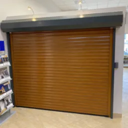 Brązowa roleta zwinięta w dół w salonie wystawowym, obok ekspozytor z katalogami.