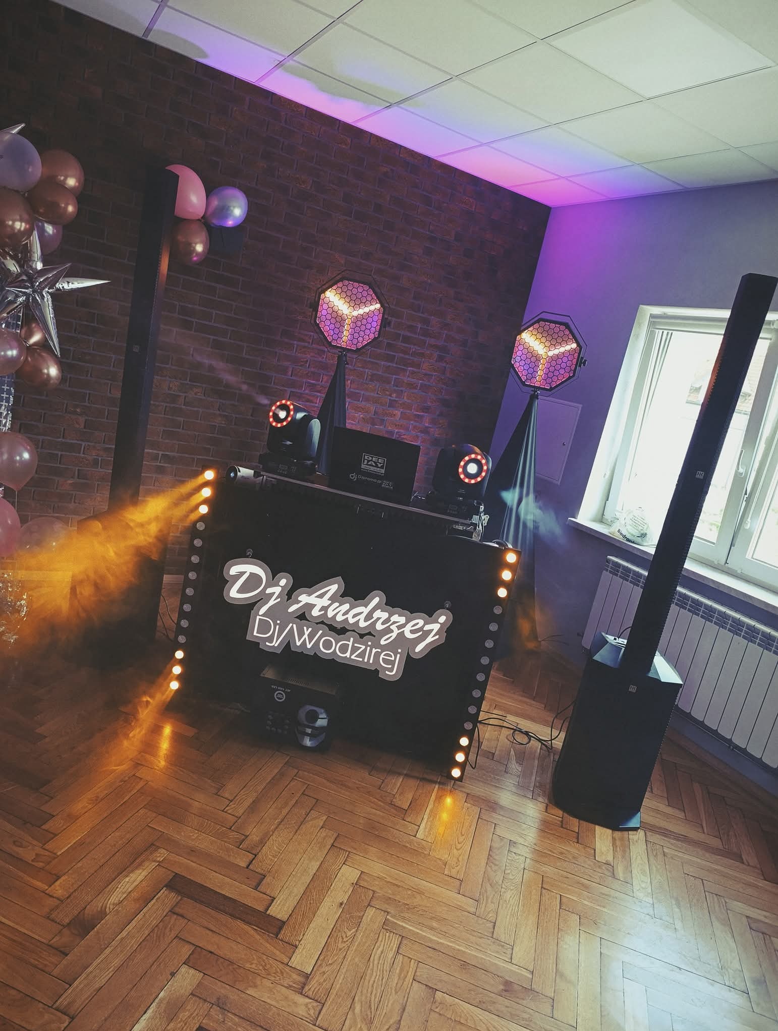 Stanowisko DJ'a z oświetleniem i nagłośnieniem, z dekoracjami balonowymi, na parkiecie z parkietem w jodełkę, przygotowane do występu.