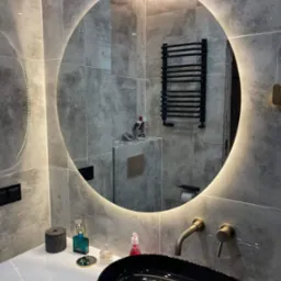 Nowoczesna łazienka z okrągłym lustrem podświetlanym LED, czarną umywalką nablatową i szarą płytką imitującą beton
