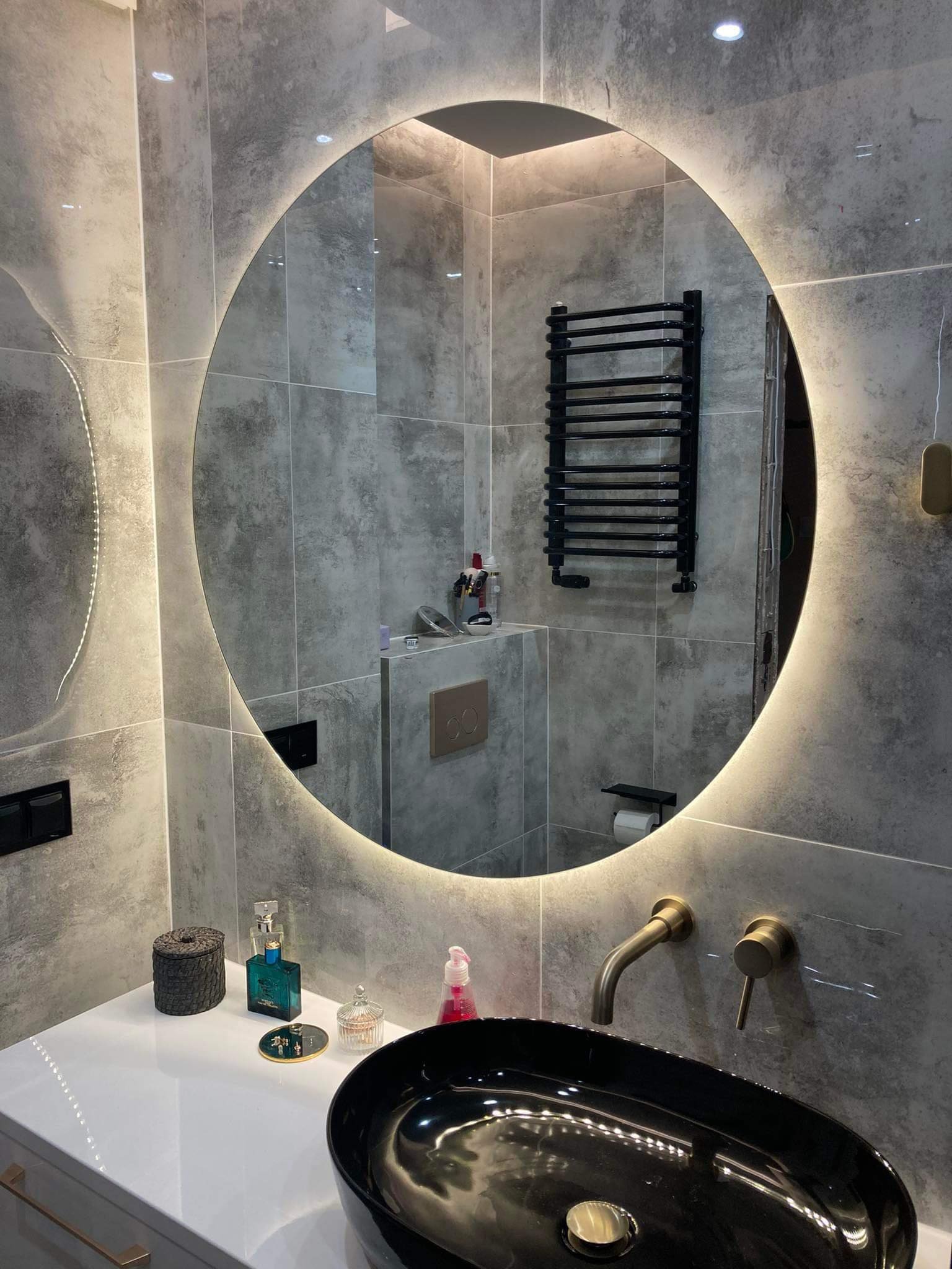 Nowoczesna łazienka z okrągłym lustrem podświetlanym LED, czarną umywalką nablatową i szarą płytką imitującą beton