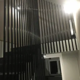 Nowoczesne schody z czarnymi, pionowymi balustradami, widok z dołu, białe ściany z dekoracyjnymi listwami, widoczny fragment kuchni w tle.