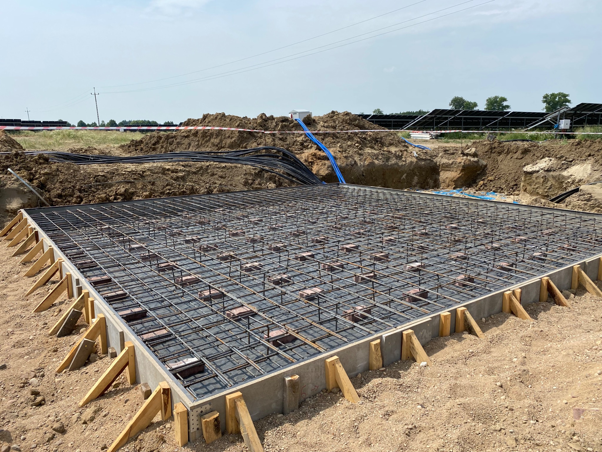 Zbrojenie fundamentu pod panele fotowoltaiczne, widoczne kable w wykopie, zabezpieczone taśmą ostrzegawczą.