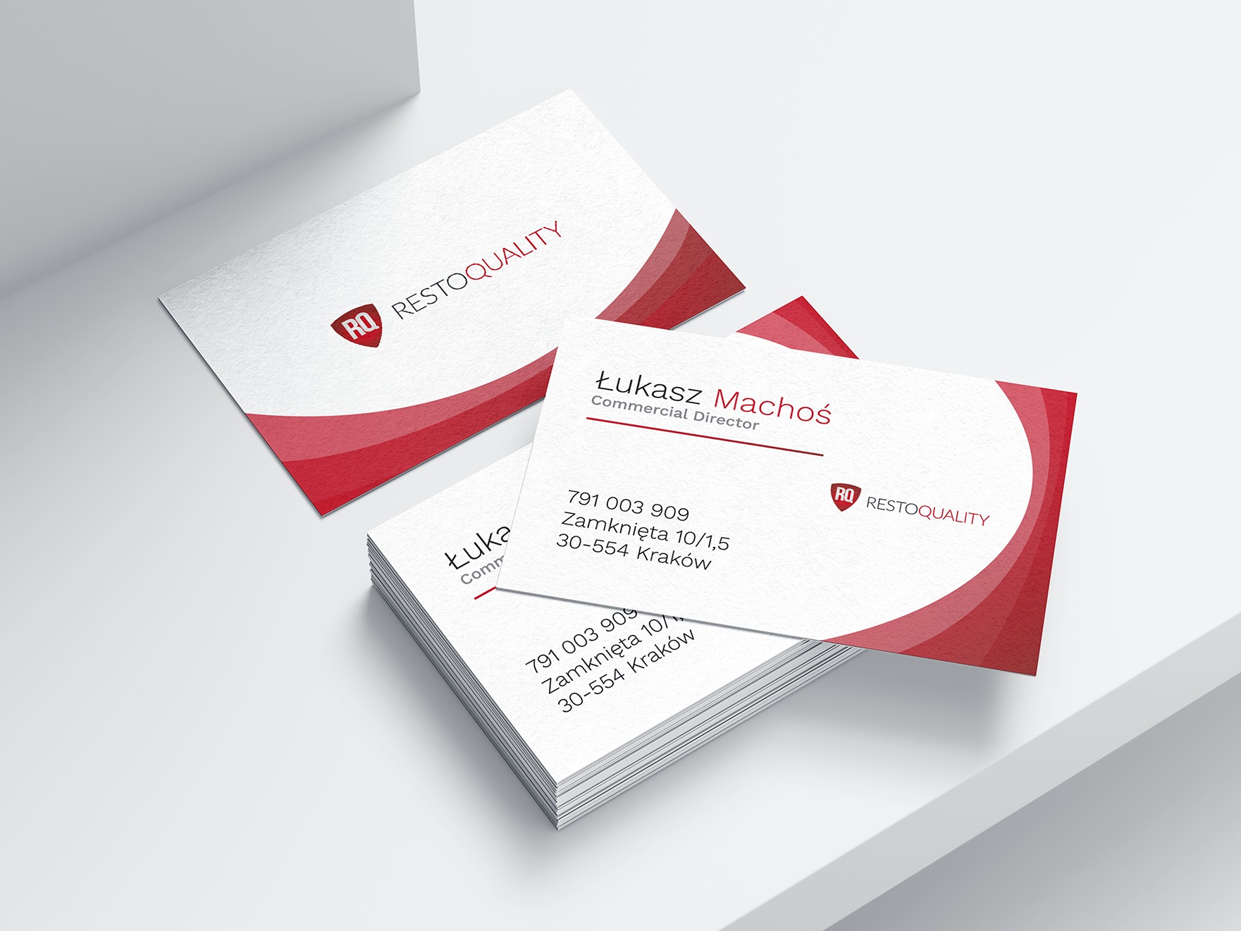 Stos wizytówek z logo i danymi kontaktowymi 'Restoquality', jedna wizytówka leży obok, całość na białym tle,  minimalistyczny design z czerwonym akcentem.