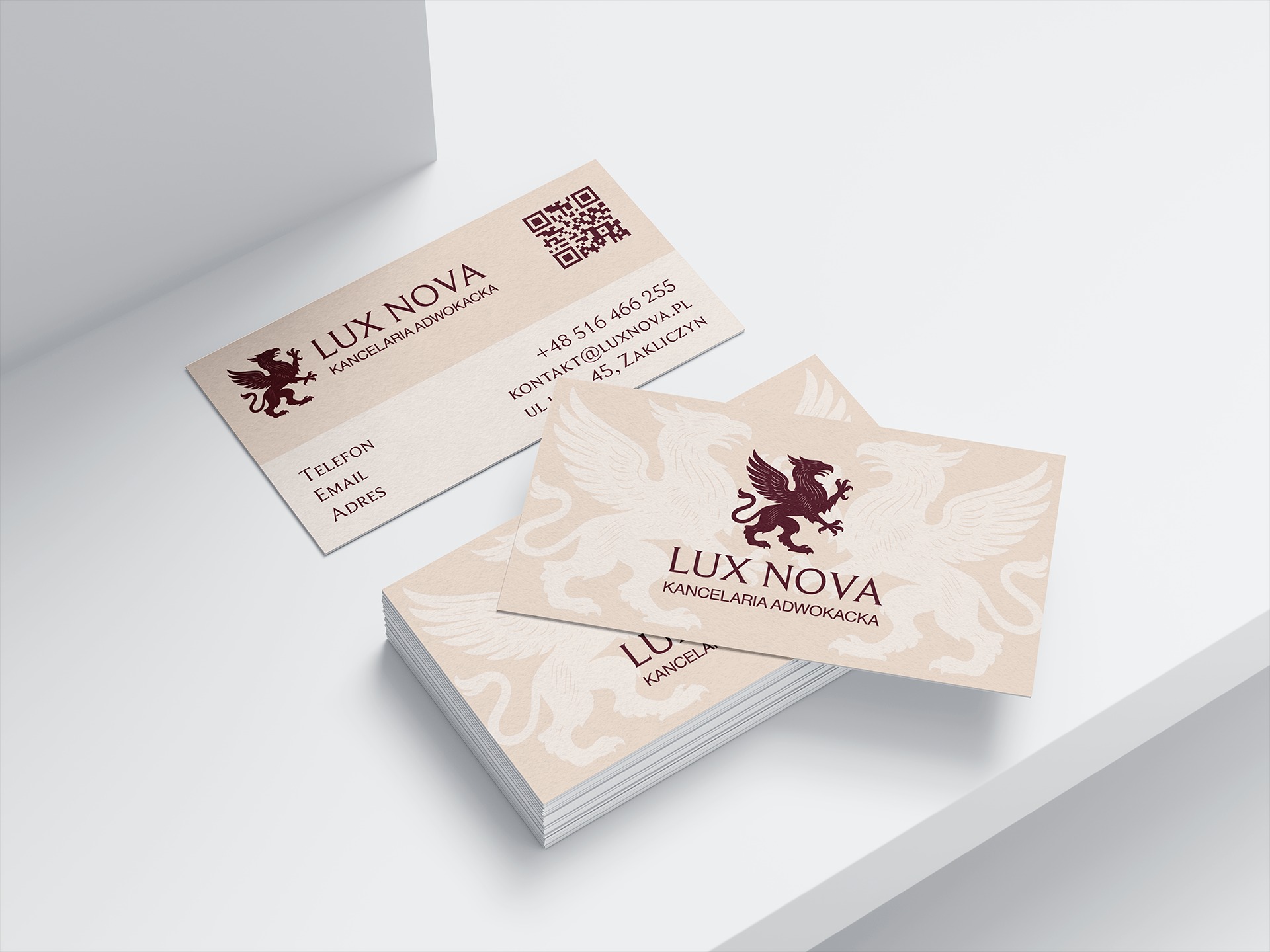 Eleganckie wizytówki kancelarii adwokackiej Lux Nova z motywem gryfa w kolorze burgundowym na beżowym tle, ułożone na białym, minimalistycznym tle.