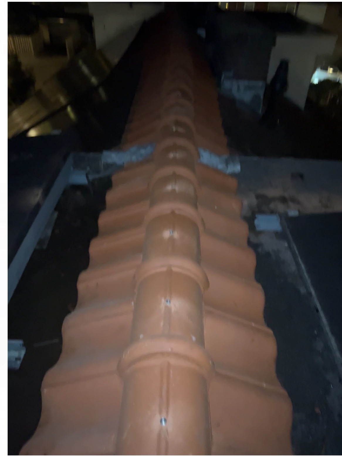 Centralne ujęcie na nową, czerwoną dachówkę karpiówkę na dachu budynku, widzianą z góry w nocnym otoczeniu. Widoczne detale mocowania.