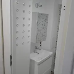 Nowoczesna, biała łazienka po remoncie z kabiną prysznicową z hydromasażem, umywalką z szafką i lustrem z mozaiką.