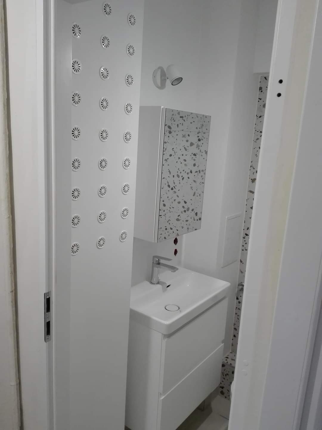 Nowoczesna, biała łazienka po remoncie z kabiną prysznicową z hydromasażem, umywalką z szafką i lustrem z mozaiką.