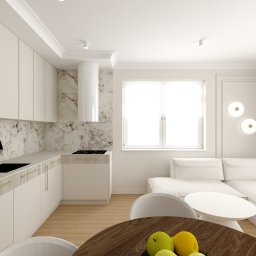 Kinga Juryś Projekty Wnętrz - Jasna kuchnia z marmurowym backsplashiem i drewnianymi akcentami. Widoczny fragment salonu z białą sofą i okrągłym stolikiem. Nowoczesny design, ciepłe oświetlenie.