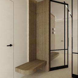 Kinga Juryś Projekty Wnętrz - Minimalistyczny przedpokój z drewnianą zabudową, siedziskiem i lustrem w czarnej ramie. Jasne ściany i podłoga, roślina w tle. Nowoczesny design.