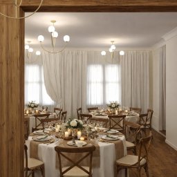 Kinga Juryś Projekty Wnętrz - Elegancka sala bankietowa z okrągłymi stołami, krzesłami z jasnego drewna i dekoracjami kwiatowymi, oświetlona nowoczesnymi lampami. Ceglana ściana w tle.