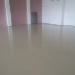 Świeżo wylana, gładka wylewka anhydrytowa w jasnym odcieniu beżu, z widocznymi refleksami światła, w surowym wnętrzu z białymi i bordowymi ścianami oraz instalacją wentylacyjną pod sufitem.