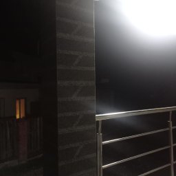 UkrPolWit - Nocne ujęcie fragmentu tarasu we Wrocławiu z kamienną kolumną o wzorzystej fakturze i metalową balustradą, oświetlonego przez lampę sufitową.