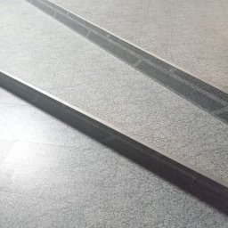 UkrPolWit - Szare płytki podłogowe z ciemnoszarymi, wpuszczonymi listwami oddzielającymi strefy, z widoczną drobną fakturą kamienia.