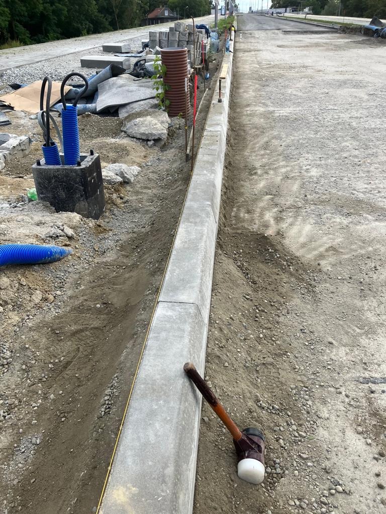 Montaż obrzeży chodnika z betonu, widoczny gumowy młotek i rów z kablami w peszlach