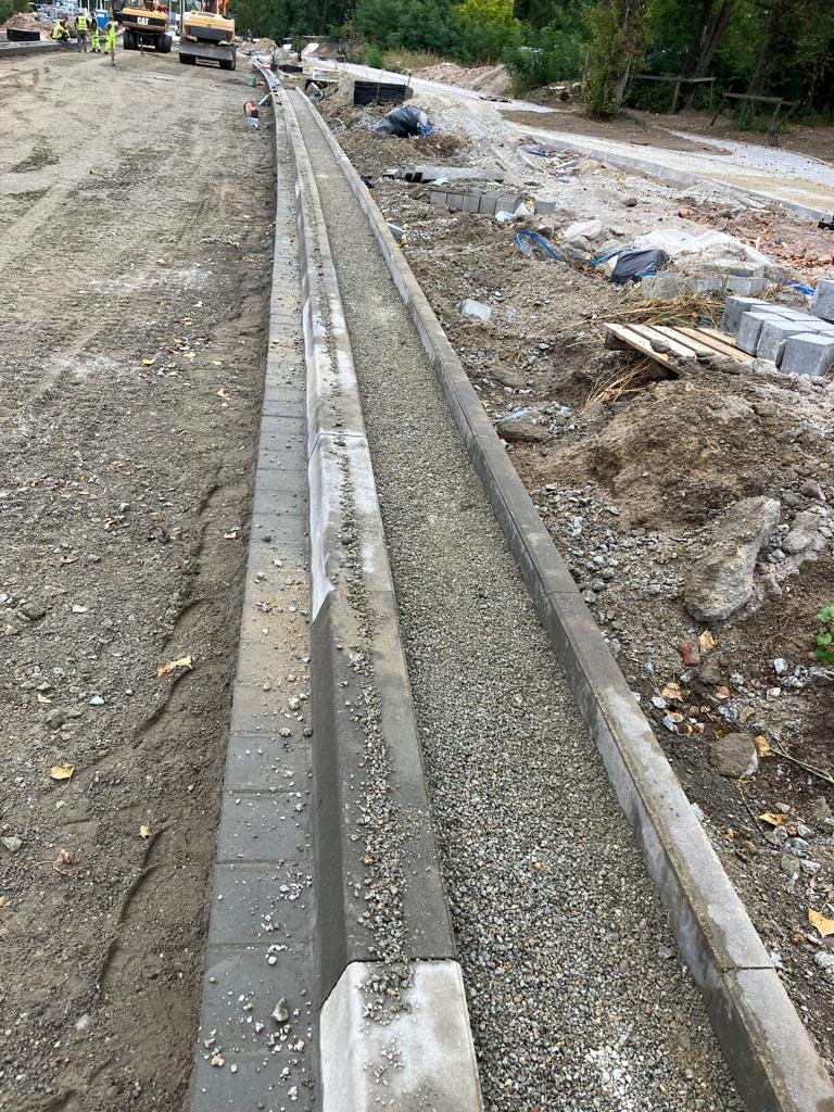 Budowa krawężnika z kostki brukowej z wypełnieniem żwirowym, ciężki sprzęt budowlany w tle